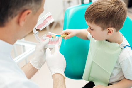 Glückliches Kind putzt Zahngebiss beim Zahnarzt
